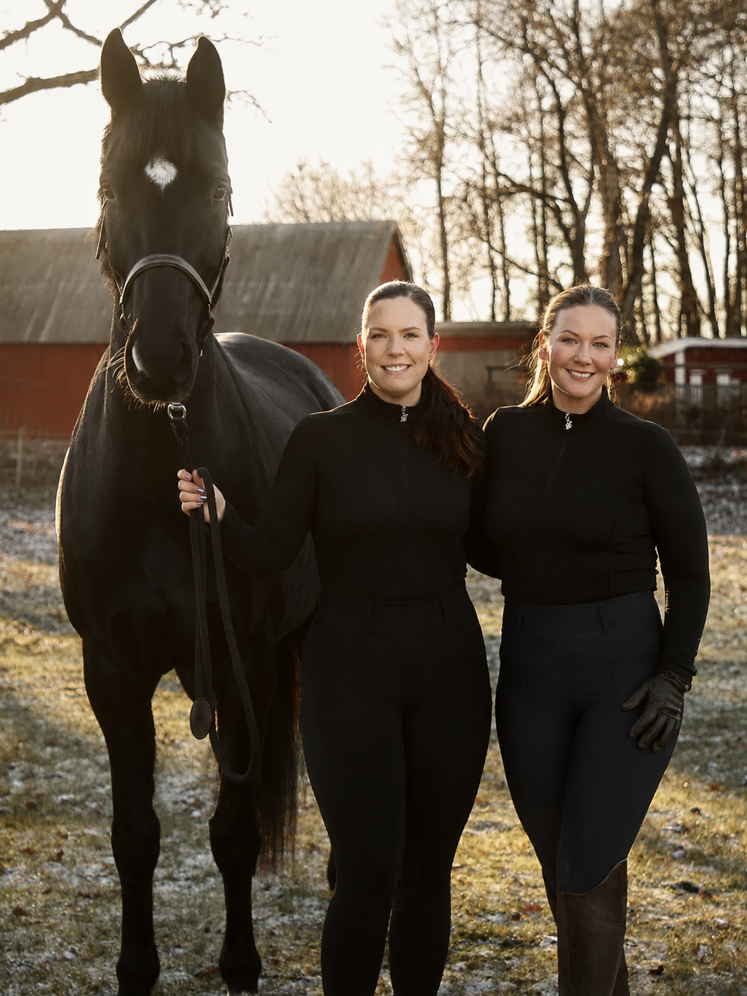 Redaktionell porträttbild av två equestrian-kreatörer bredvid en grå häst i en solig stallgång
